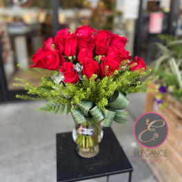 Red roses arranged in a glass vase with a green ribbon bow