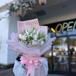 Pink-wrapped bouquet of white tulips with a striped ribbon