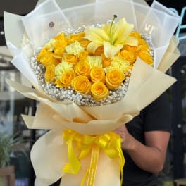 Yellow rose bouquet with lilies and white filler flowers wrapped in cream paper