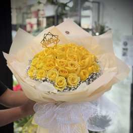 Bouquet of yellow roses wrapped in cream paper with a white ribbon