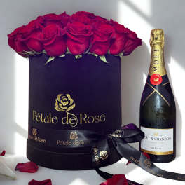 Black hat box of red roses beside a champagne bottle with scattered rose petals.