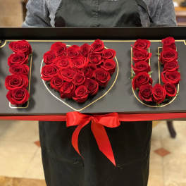 Red roses arranged to spell I love you in a black gift box