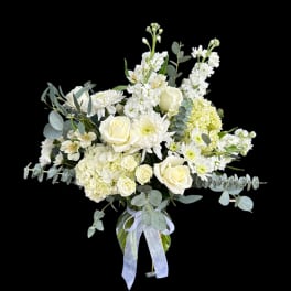 White roses and mixed white flowers in a glass vase with a ribbon
