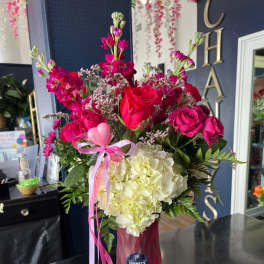 Pink and white floral arrangement in a pink vase with ribbon