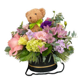 Teddy bear in a flower arrangement with pink and purple blooms in a black hatbox