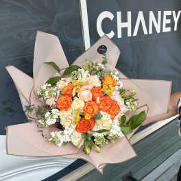 Bouquet of orange and cream roses with white filler flowers in pink wrap