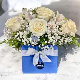 Cream roses and small white filler flowers in a blue gift box with a white ribbon