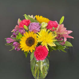 Mixed bouquet of sunflowers, lilies, roses, and carnations in a glass vase