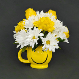 Yellow smiley-face mug filled with white daisies, yellow daisies, and yellow roses on a dark background