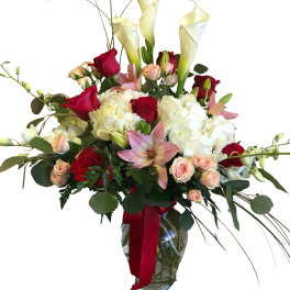 Tall bouquet of white calla lilies, red roses, and pink lilies in a glass vase