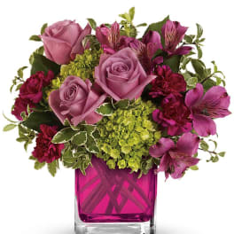Compact bouquet of mauve roses and hot pink blooms in a bright pink glass cube vase