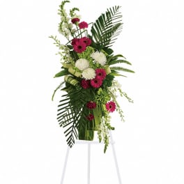 Tall standing spray of hot pink gerbera daisies and white mums with palms on a white easel stand