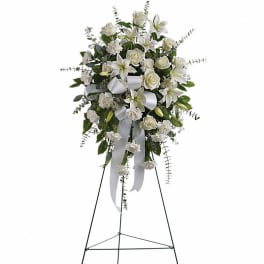 Tall white standing spray with lilies, roses, and carnations on a metal easel with white bow