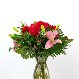 Bouquet of red roses, pink lilies, and red carnations in a glass vase