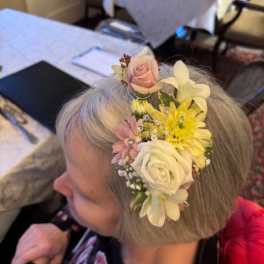 Floral hairpiece with pink, white, and yellow flowers worn in gray hair
