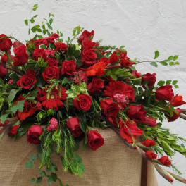 Large red rose arrangement with mixed greenery on a burlap-draped stand