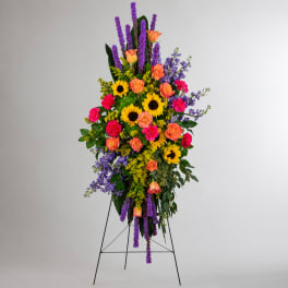 Tall standing floral spray with sunflowers, roses, and purple flowers on an easel