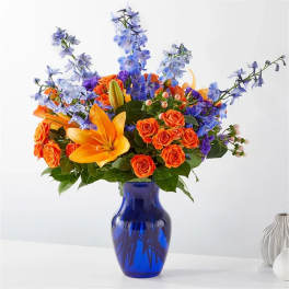 Orange roses and lilies with blue flowers in a cobalt vase