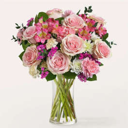 Pink roses and mixed blooms arranged in a clear glass vase