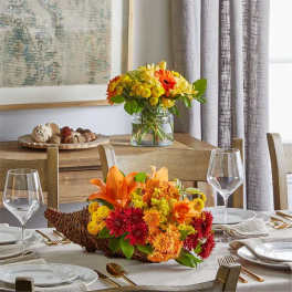 Two autumn floral centerpieces with orange and yellow blooms on a dining table