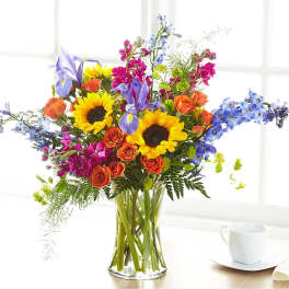 Mixed bouquet with sunflowers, roses, irises, and blue flowers in a glass vase