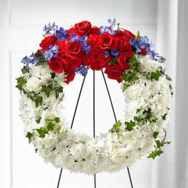 Red rose and white chrysanthemum wreath with blue accents on a stand