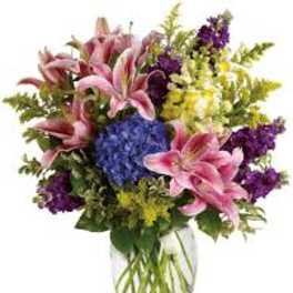 Bouquet of pink lilies, blue hydrangea, and purple flowers in a glass vase