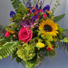 Mixed bouquet with a pink rose, sunflower, and purple blooms in a glass vase