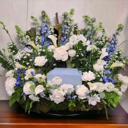 Large floral funeral arrangement with white roses, calla lilies, and blue flowers
