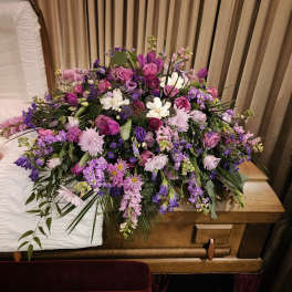 Large purple and pink floral spray on a wooden casket