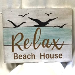 Wooden sign reading Relax Beach House with bird silhouettes