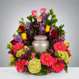 Colorful funeral urn surround with roses, gerberas, and hydrangeas
