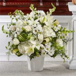 White floral arrangement in a white vase with lilies, roses, and daisies