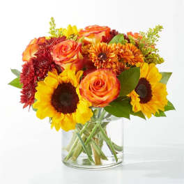 Bouquet of sunflowers, orange roses, and mums in a clear glass vase