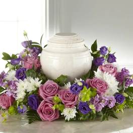 Purple and pink floral arrangement surrounding a white urn
