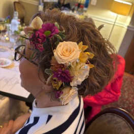 Floral hairpiece with cream roses and purple flowers worn in a woman's hair
