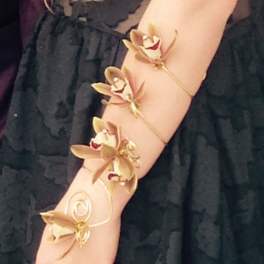 Arm wearing a gold orchid bracelet over a black dress
