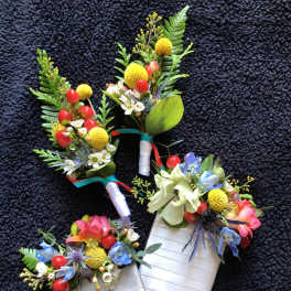 Three floral boutonnieres with colorful blooms and ribbon-wrapped stems