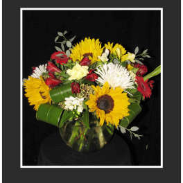 Mixed bouquet with sunflowers, red gerberas, and white blooms in a glass vase