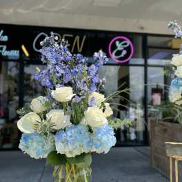 Tall bouquet of blue hydrangeas, white roses, and purple flowers in a glass vase
