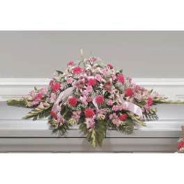 Pink and white floral casket spray with ribbon on a white casket