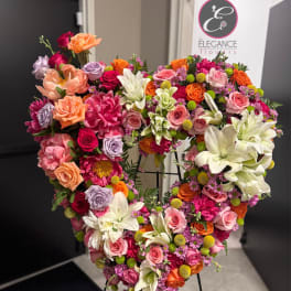 Heart-shaped floral wreath with roses, lilies, and pink accents on an easel