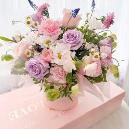 Pink and lavender bouquet with roses, carnations, and daisies in a round box