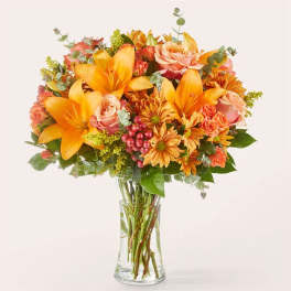 Bouquet of orange lilies, roses, and daisies in a clear glass vase