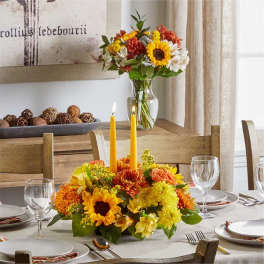 Sunflower and chrysanthemum centerpiece with two yellow candles on a dining table
