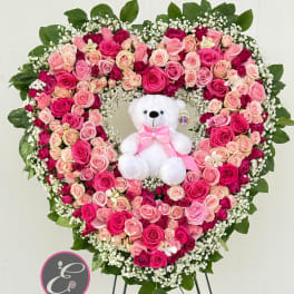 Heart-shaped pink rose arrangement with a white teddy bear in the center