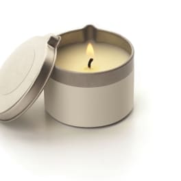 Lit candle in a round metal tin with the lid beside it