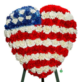 Heart-shaped floral display of red, white, and blue carnations in a flag design on a stand