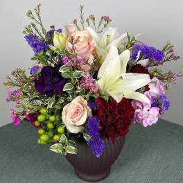 Mixed bouquet with roses, lilies, and purple filler flowers in a vase