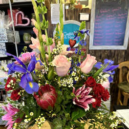 Mixed bouquet of pink, red, and blue flowers in a glass vase